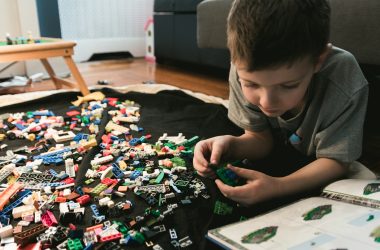 boy in grey crew-neck t-shirt plays LEGO bricks with white manual book